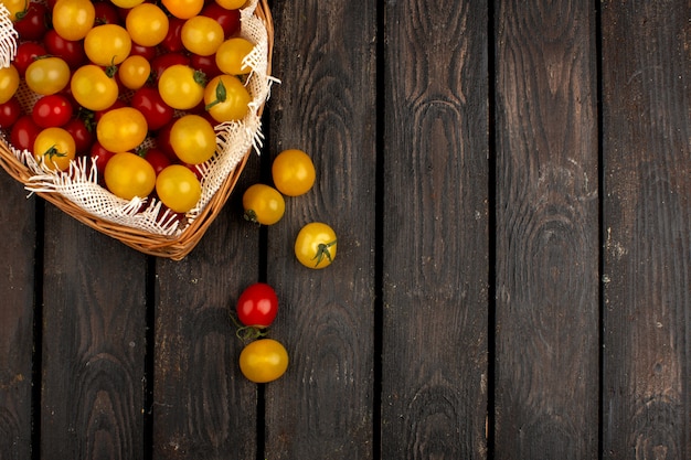 Tomates amarillos y rojos frescos maduros dentro de la canasta en el piso rústico de madera