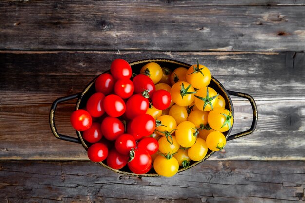 Tomates amarillos y rojos en una olla sobre un fondo oscuro de la madera. vista superior.