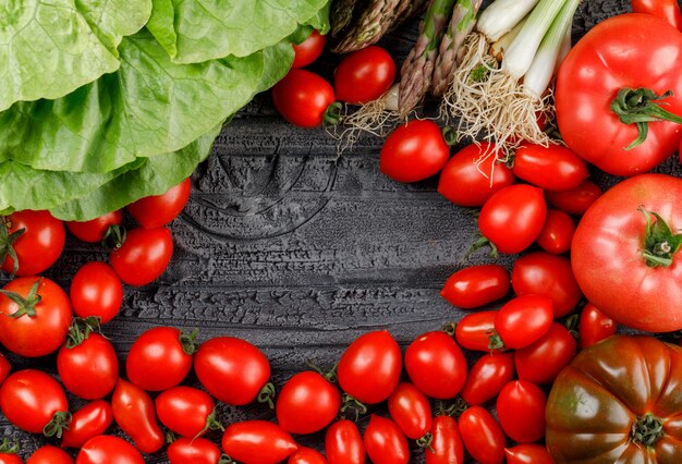 Los tomates se apilan con lechuga, espárragos, cebollas verdes en una pared de madera gris