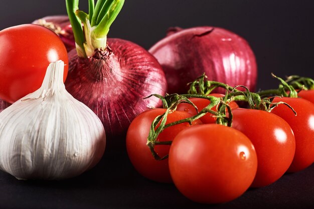 Los tomates, las cebollas y el ajo se aíslan en un negro