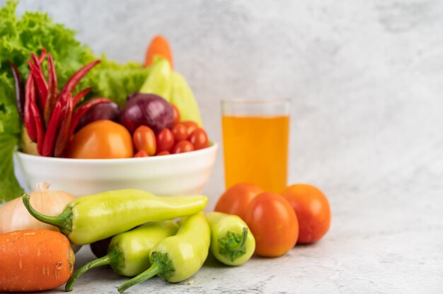 Tomates, cebollas rojas, pimientos, zanahorias y col china en una taza blanca en el piso de cemento.