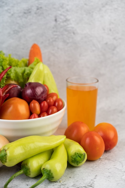 Tomates, cebollas rojas, pimientos, zanahorias y col china en una taza blanca en el piso de cemento.