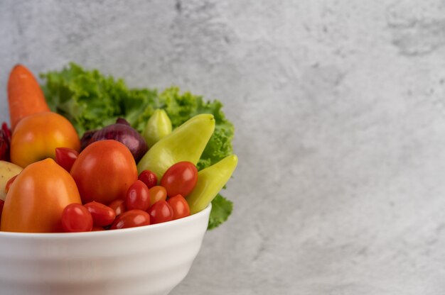 Tomates, cebollas rojas, pimientos, zanahorias y col china en una taza blanca en el piso de cemento.