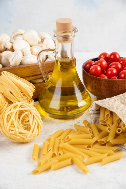 Tomates cherry con aceite de oliva, champiñones y pastas crudas sobre el mármol.