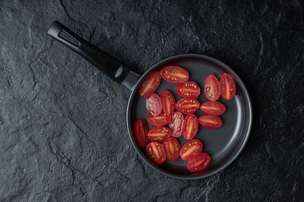 Tomates cherry frescos cortados a la mitad en una sartén negra sobre fondo negro.