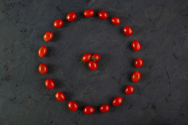 Tomates cherry frescos maduros y suaves vitaminas ricas en forma de pequeños tomates cherry rojos en forma de escritorio oscuro