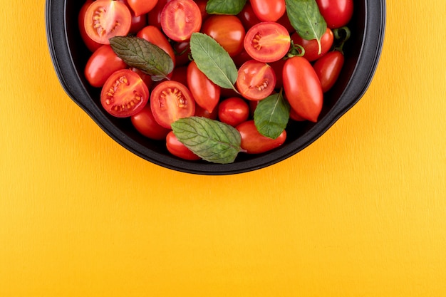 Tomates cherry y hojas de menta en un tazón negro sobre la superficie amarilla vista superior con espacio de copia