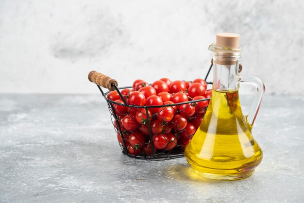 Tomates cherry rojos con una botella de aceite de oliva virgen extra sobre mesa de mármol.