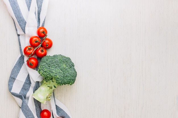 Tomates cherry rojos y brócoli sobre la toalla contra superficie de madera