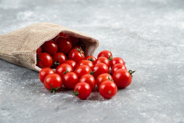 Tomates cherry rojos de una canasta rústica sobre mesa de mármol.