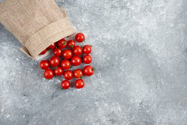 Tomates cherry rojos de una canasta rústica sobre mesa de mármol.