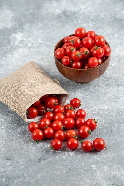 Tomates cherry rojos de una canasta rústica y en una taza de madera sobre una mesa de mármol.