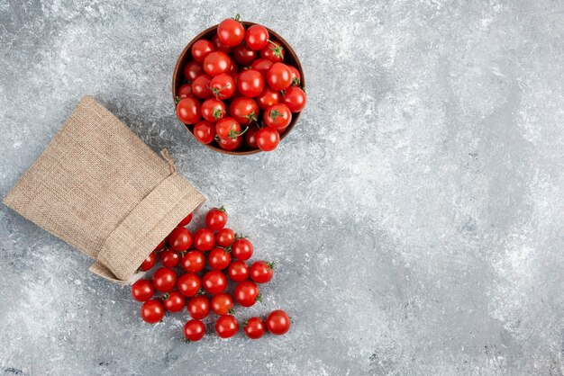 Tomates cherry rojos de una canasta rústica y en una taza de madera sobre una mesa de mármol.