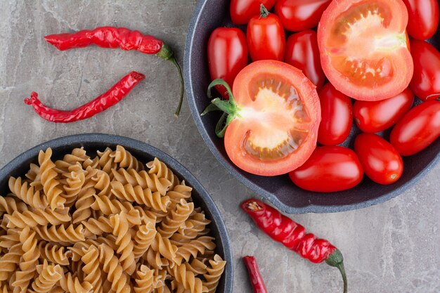 Tomates cherry rojos y chiles en una sartén con pastas alrededor.