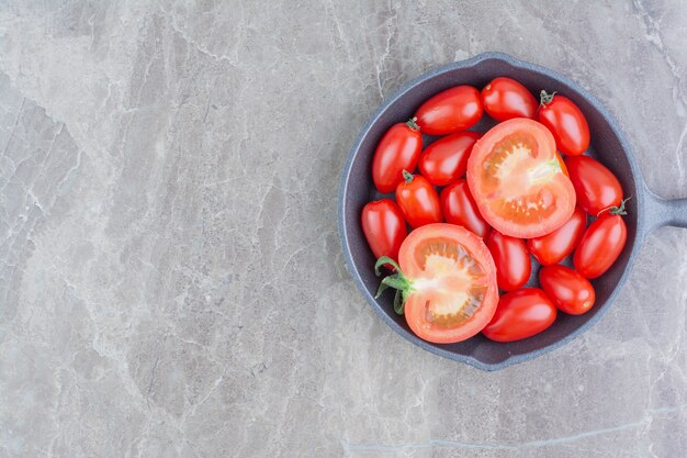 Tomates cherry rojos enteros y medio cortados en una sartén negra