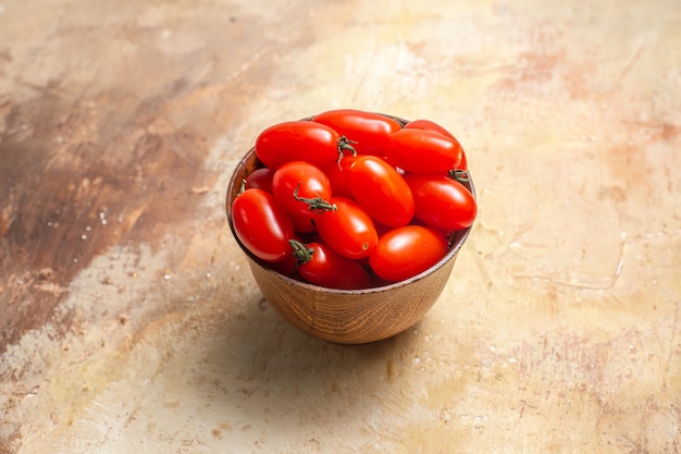 Tomates cherry de vista frontal en un tazón de madera sobre fondo ámbar con espacio libre