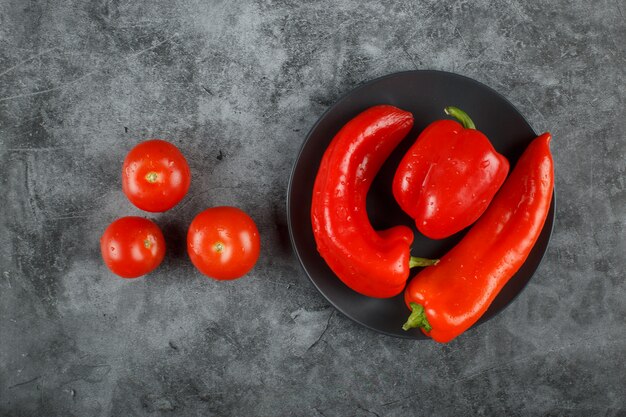 Tomates y chiles en un plato negro y sobre la mesa. Vista superior.