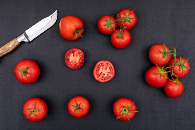 Tomates completos y medios y cerca del cuchillo sobre superficie negra