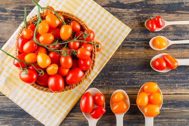 Tomates en cucharas de madera y cestas planas sobre tela de madera y picnic