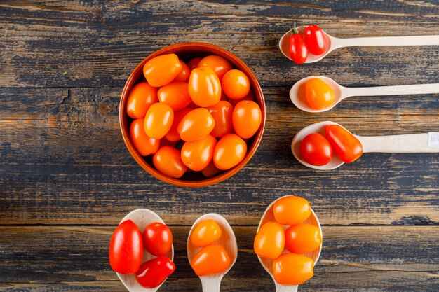 Tomates en cucharas de madera y tazón de fuente en una mesa de madera. aplanada