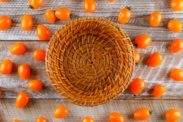 Tomates dispersos con la cesta vacía plana yacía sobre una mesa de madera