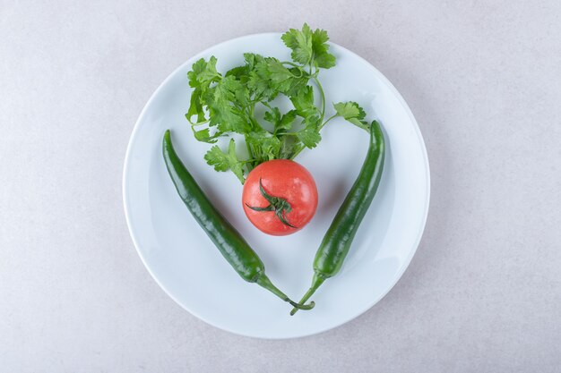 Tomates enteros, chiles y perejil en un plato sobre una mesa de mármol.