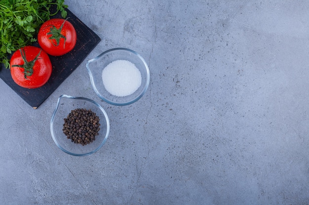 Foto gratuita tomates frescos y hojas de perejil sobre una tabla de cortar negra con condimentos.