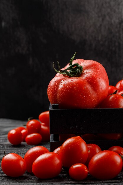 Tomates fríos en una caja de madera en la pared gris y oscura, vista lateral.