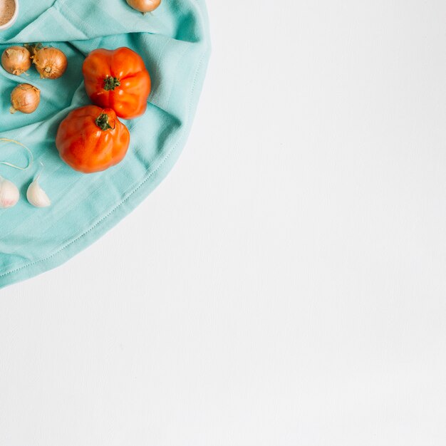 Tomates de la herencia con la cebolla y los dientes de ajo en servilleta azul contra el fondo blanco