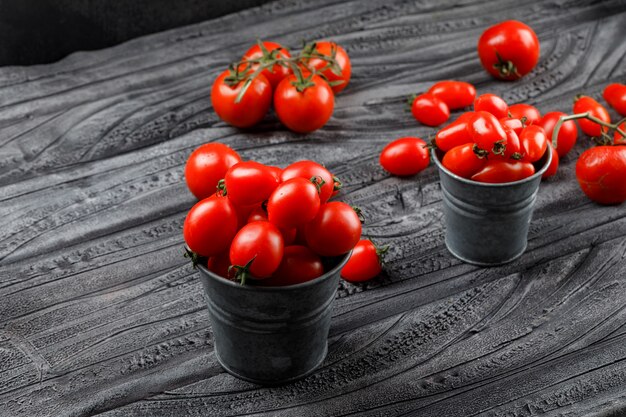 Tomates maduros en mini cubos en madera gris y pared negra. Vista de ángulo alto.