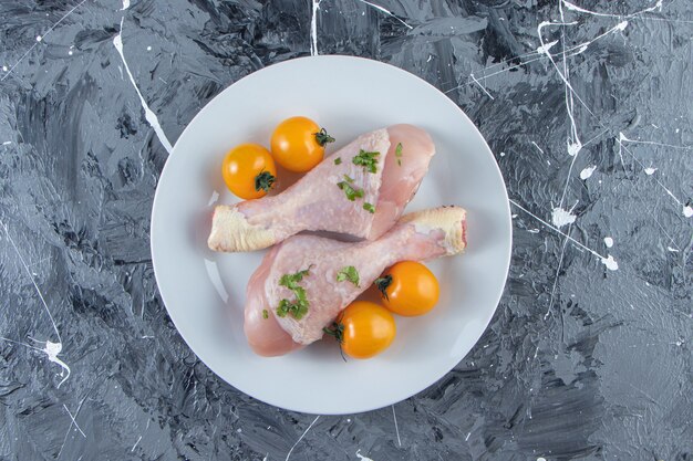 Tomates naranjas y muslos de pollo en un plato, sobre la superficie de mármol.