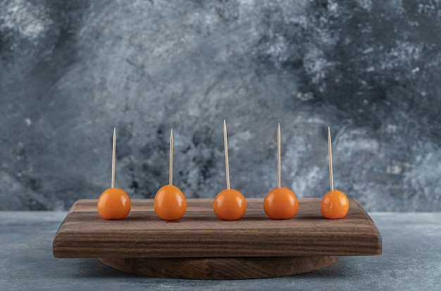 Tomates naranjas con palos sobre tabla de madera.