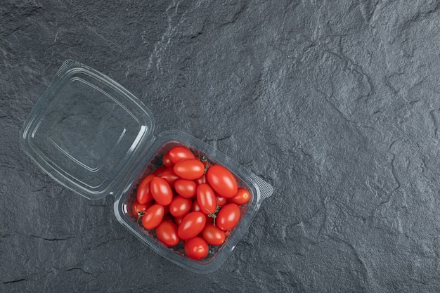 Tomates pequeños rojos en recipiente de plástico sobre fondo negro. Foto de alta calidad