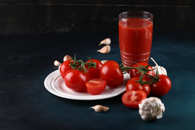Tomates en plato blanco con guantes de ajo y un vaso de jugo de tomate.