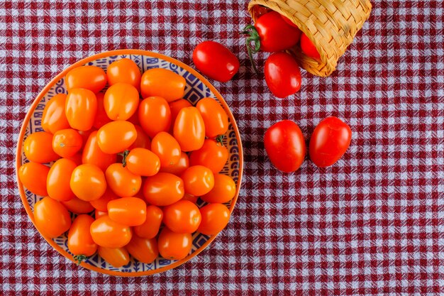 Los tomates en un plato y una canasta planos yacían sobre una tela de picnic