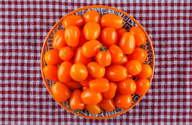 Tomates en un plato sobre tela de picnic, plana.