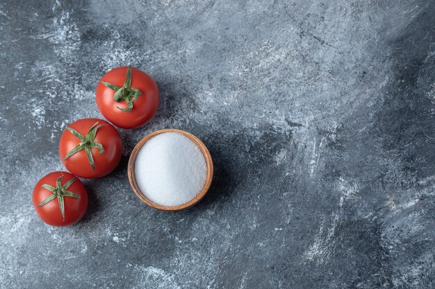 Tomates rojos frescos con un cuenco de madera lleno de sal.