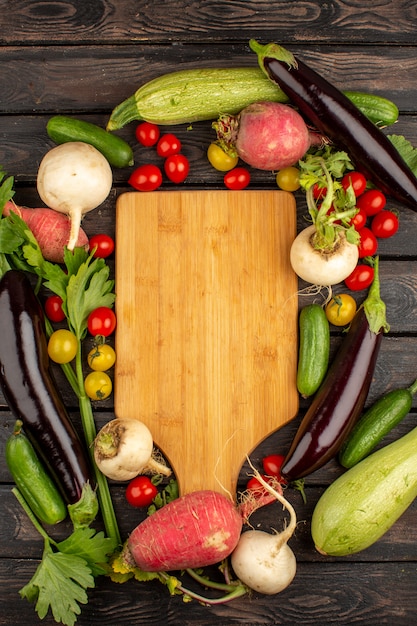 Tomates rojos frescos y maduros otros vegetales como rábano rojo y berenjenas negras en un piso rústico de madera