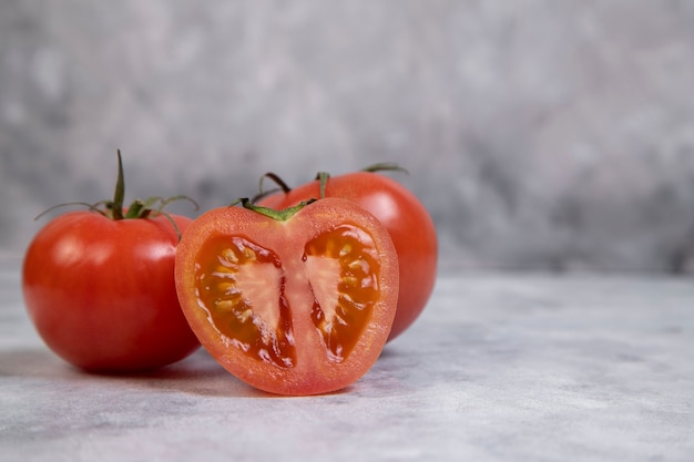 Tomates rojos jugosos enteros y en rodajas colocados sobre mármol