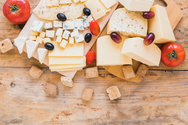 Tomates rojos, uvas, aceitunas y bloques de queso en el escritorio de madera