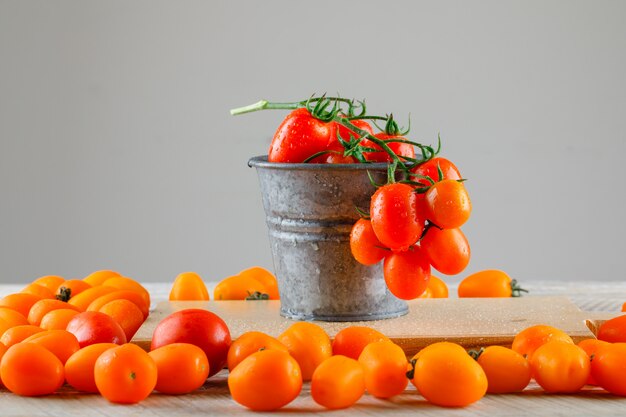 Tomates con tabla de cortar en un mini cubo en la mesa de madera, vista lateral.