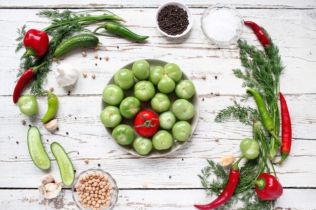 Tomates verdes, encurtidos en mesa de madera blanca con pimientos verdes y rojos y chiles, hinojo, sal, pimienta negra, ajo, guisantes, primer plano, concepto saludable, vista superior, endecha plana