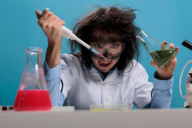 Foto gratuita una tonta y tonta trabajadora de laboratorio con pipeta y frasco de vidrio mezclando compuestos químicos tóxicos para crear una nueva fórmula. loco científico loco mezclando sustancias líquidas mientras sonríe terriblemente.