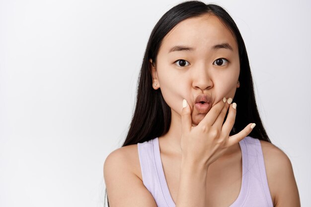 Tonto joven mujer asiática hurgando y apretando su cara labios fruncidos lindo haciendo divertido adorable expresión facial fondo blanco.