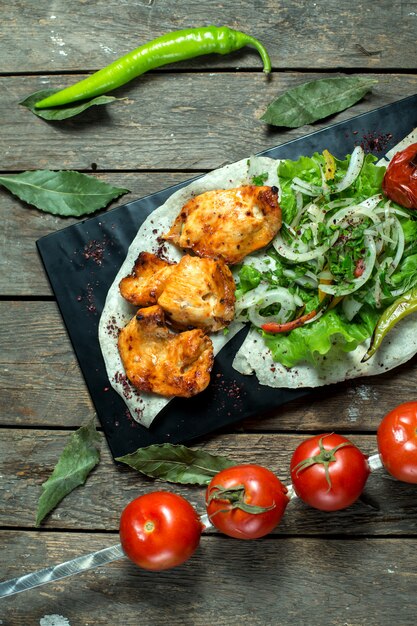 top kebab de pollo servido con cebolla hierbas frescas tomate asado y pimiento en pizarra