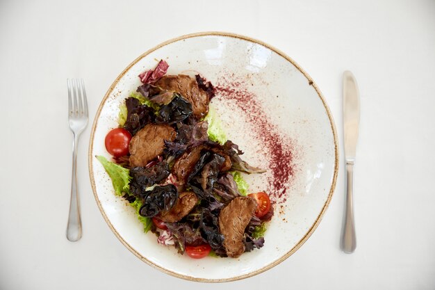 Topview de ensalada de carne servida con tomates cherry y lechuga en la mesa blanca