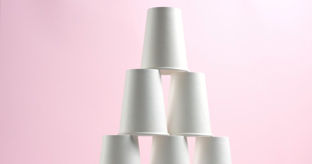 Torre hecha de vasos de papel blanco sobre fondo rosa