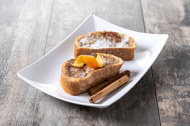 Torrijas caseras tradicionales españolas decoradas con canela y cáscara de naranja sobre mesa de madera