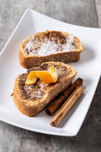 Torrijas caseras tradicionales españolas decoradas con canela y cáscara de naranja sobre mesa de madera