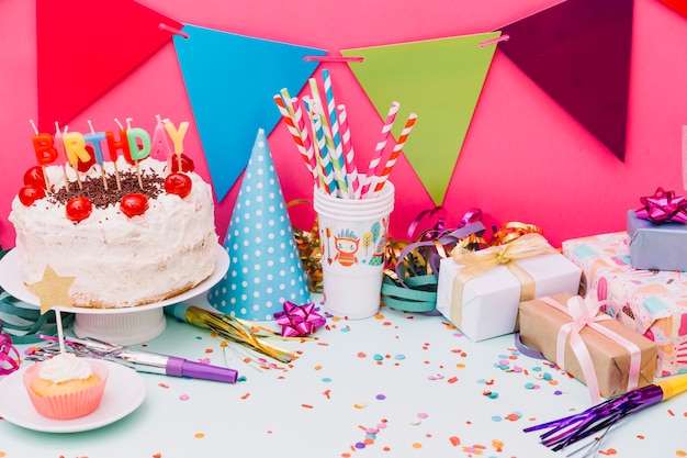 Torta de cumpleaños con accesorios de fiesta y confeti sobre fondo azul